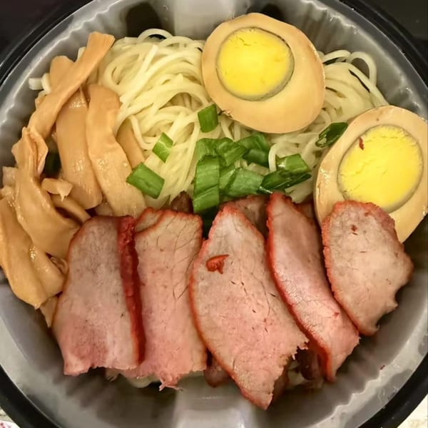 Asian Arch's ramen bowl with noodles, sliced pork, bamboo shoots, green onions, and two halved eggs.
